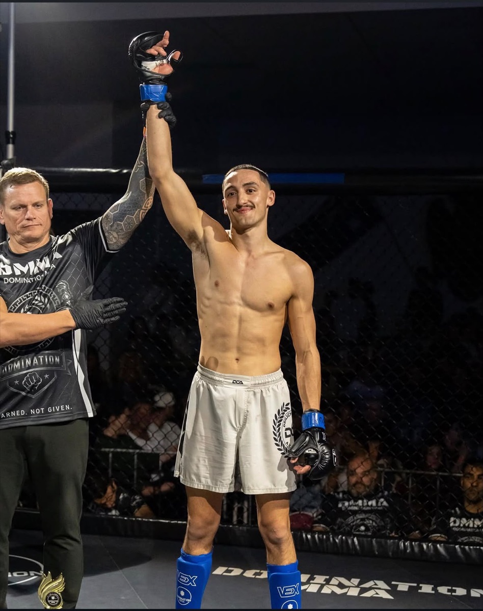 A DCA member in DCA fight shorts has his hand raised after winning in the cage