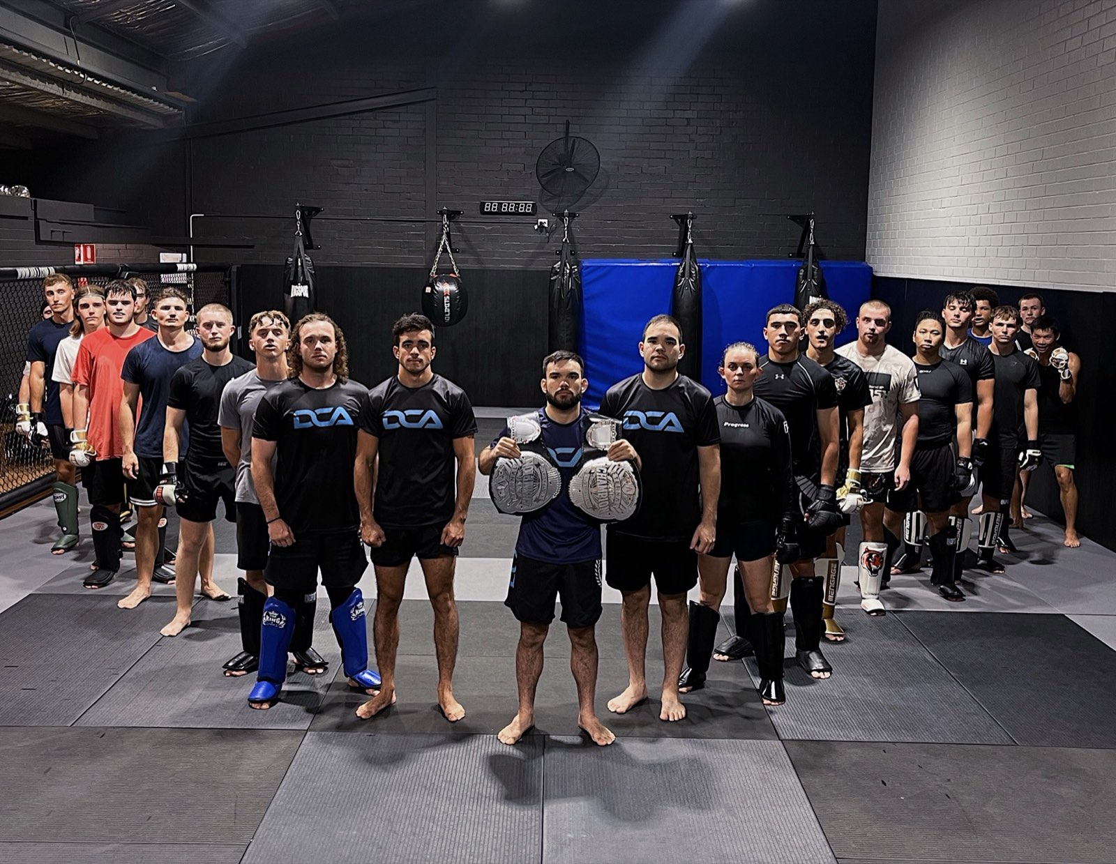 The DCA MMA team lined up on the mats with championship belts